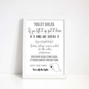 May include: A framed white print with black text that reads "TOILET RULES." The text includes instructions such as "If you lift it up, put it down" and "Wash your hands." A simple illustration of a toilet paper roll is included.