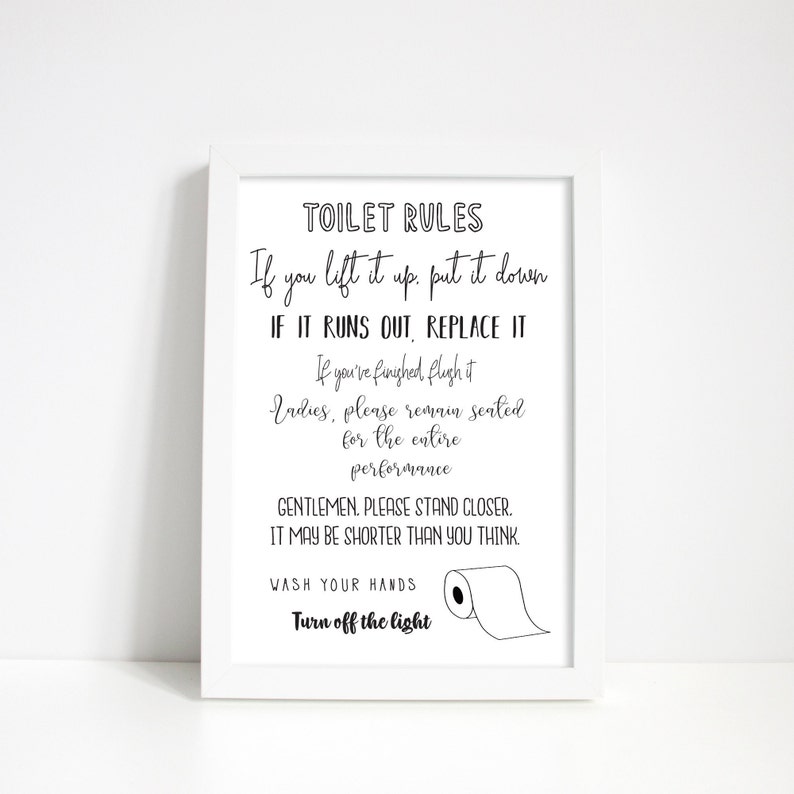 May include: A framed white print with black text that reads "TOILET RULES." The text includes instructions such as "If you lift it up, put it down" and "Wash your hands." A simple illustration of a toilet paper roll is included.