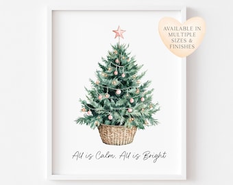 May include: A framed wall art print featuring a watercolor illustration of a green Christmas tree in a woven basket, topped with a pink star and decorated with pink ornaments. The text reads: All is Calm. All is Bright.