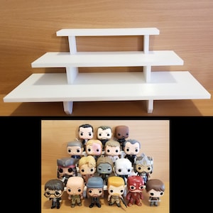 May include: White three-tiered shelf unit with a collection of pop culture figurines on the bottom shelf. The figurines are mostly male characters with a few female characters. The figurines are all in a standing position.