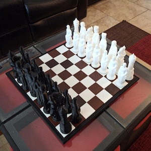 May include: A black and white chess set with black pieces on a brown and white chessboard. The white pieces are made of white plastic and the black pieces are made of black plastic.