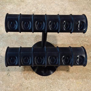 May include: Black jewelry stand with two tiers, each with six circular slots for holding bracelets. The slots are decorated with a repeating pattern of a stylized Mickey Mouse head.