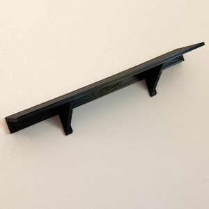 May include: A black shelf with two triangular brackets on a white wall.