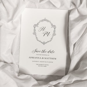 May include: Save the date card with a decorative monogram of "AM" in a circle with a floral design. The card announces the wedding of Adrianna and Matthew on Saturday, August 21 at 4:00 PM at the Marriott Hotel, Rue de Paris.
