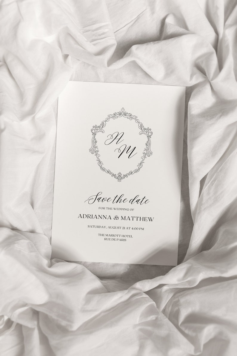 May include: Save the date card with a decorative monogram of "AM" in a circle with a floral design. The card announces the wedding of Adrianna and Matthew on Saturday, August 21 at 4:00 PM at the Marriott Hotel, Rue de Paris.
