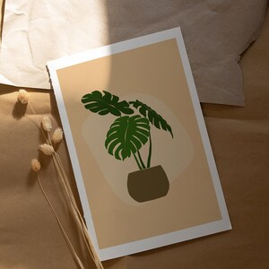 Peut inclure: Une impression d'une plante de monstera verte dans un pot brun sur un fond brun clair.