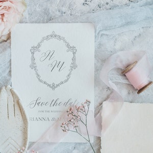 May include: A white save the date card with a decorative border and the initials "H & M" in cursive. The text "Save the date for the wedding of Rianna & Matt" is printed below the initials.