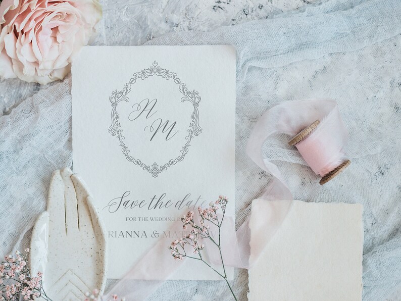 May include: A white save the date card with a decorative border and the initials "H & M" in cursive. The text "Save the date for the wedding of Rianna & Matt" is printed below the initials.