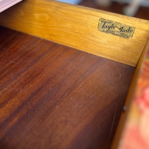 以下が含まれることがあります： 木製の引き出しのクローズアップ。引き出しには「Taylor-Made Bedford Furniture」と書かれた金色のラベルが付いています。