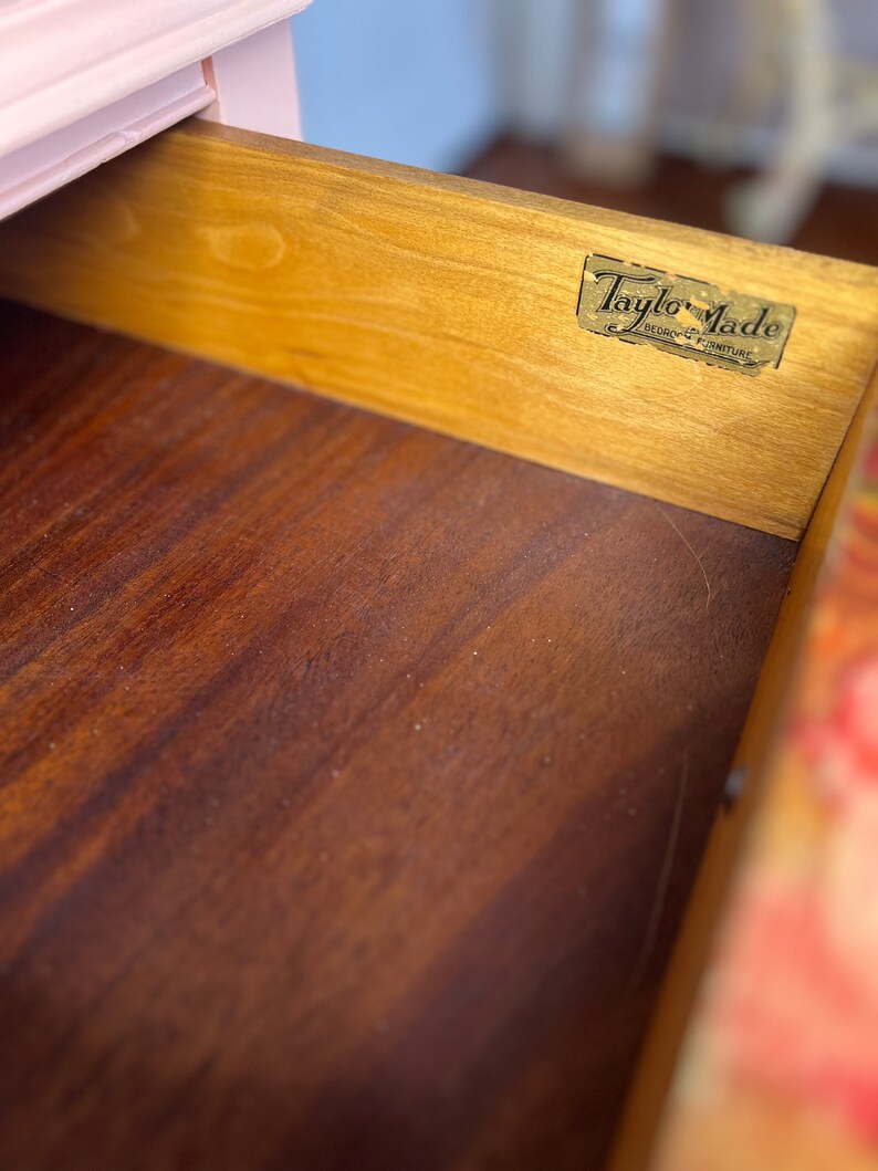 以下が含まれることがあります： 木製の引き出しのクローズアップ。引き出しには「Taylor-Made Bedford Furniture」と書かれた金色のラベルが付いています。