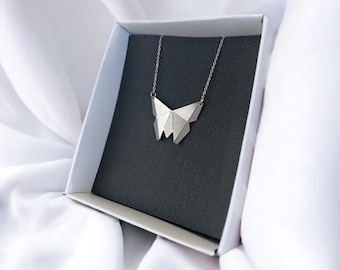 May include: A silver geometric butterfly necklace in a white box with a black interior.