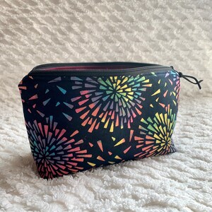 May include: A black zippered pouch with a colorful firework pattern. The pouch is made of fabric and has a zipper closure.
