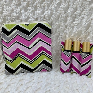 May include: A set of two zippered pouches with a chevron pattern in shades of pink, green, black, and gray. The larger pouch has a zipper closure and a braided tassel. The smaller pouch has three slots for holding essential oil bottles.