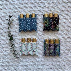 May include: Four fabric pouches with different patterns, each holding three gold roller bottles. The pouches are designed to hold essential oils or other small items.
