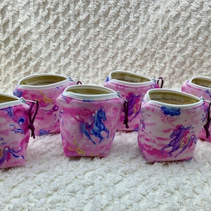 May include: Five pink zippered pouches with a unicorn and cloud print. The pouches have a white zipper and a purple drawstring.