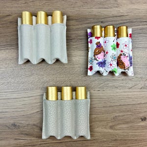 May include: Three different fabric pouches for essential oil roller bottles. The pouches are beige, white with a floral pattern, and gray with white polka dots. Each pouch has four slots for the bottles.