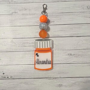 Puede incluir: Llavero de botella de píldoras naranja y plateado con el nombre Alexandria en la etiqueta.