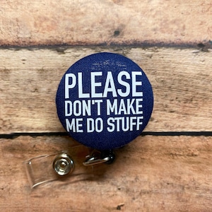 May include: A blue button with white text that reads "PLEASE DON'T MAKE ME DO STUFF". The button is attached to a clear plastic retractable badge holder.