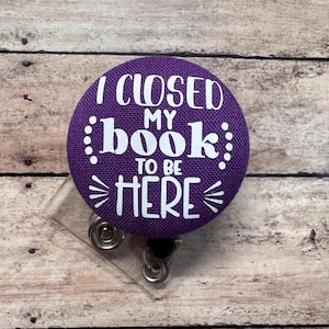 May include: Purple fabric badge holder with a white text that reads "I closed my book to be here".