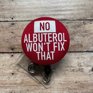 May include: Red button badge with white text that reads "NO ALBUTEROL WON'T FIX THAT". The badge is attached to a retractable badge holder.
