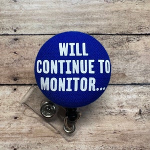 May include: Blue round badge with white text that reads "WILL CONTINUE TO MONITOR..." attached to a clear plastic badge holder with a black retractable cord.