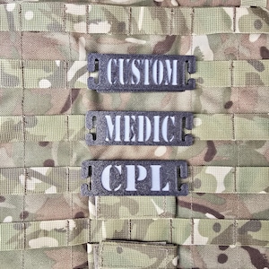 Op de afbeelding: Drie zwarte klittenbandpatches met witte tekst. De bovenste patch zegt "CUSTOM", de middelste patch zegt "MEDIC" en de onderste patch zegt "CPL".