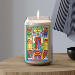 May include: A white candle with a blue and yellow label featuring a religious icon of a woman in a red and blue robe. The label also includes the text "Kidin Asena".