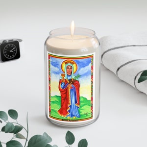 May include: A white candle in a glass jar with a colorful image of Saint Teklehaimanot, a Christian saint, holding a chalice and a palm branch. The image is surrounded by a red, yellow, and green border. The text "Saint Teklehaimanot" is printed below the image.