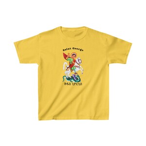 May include: Yellow t-shirt with a graphic of Saint George slaying a dragon on horseback. The text "Saint George" and "ቅዱስ ጊዮርጊስ" is printed on the shirt.