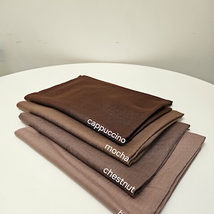 May include: Four different shades of brown fabric swatches stacked on top of each other. The swatches are labelled from top to bottom: cappuccino, mocha, chestnut, and hazelnut.
