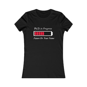 May include: Black women's t-shirt with white text that reads "Ph.D. in Progress" and a battery icon with a red progress bar. The text below the battery icon reads "Future Dr. Your Name".