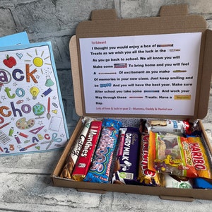 May include: A gift box containing assorted chocolate bars and sweets, such as Galaxy and Haribo. A handwritten message is inside the box. A colourful "Back to School" card is visible on the left.