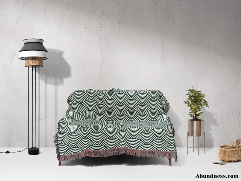 May include: A living room setting with a sofa covered by a green and white patterned throw. A black and white floor lamp is on the left, and a plant in a gold stand is on the right. The word "Abundance" is at the bottom of the image.