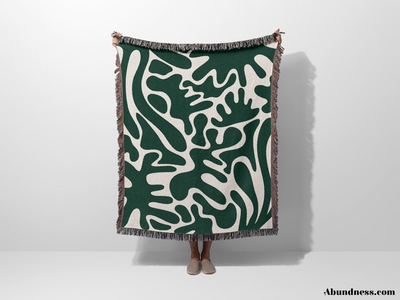 May include: A green and white woven throw blanket with an abstract pattern of organic shapes. The blanket has a fringe border.