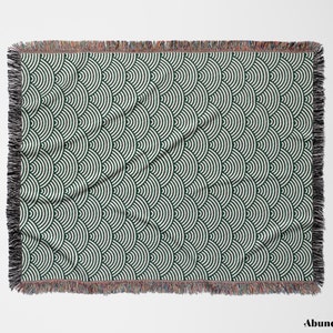 May include: A rectangular throw blanket featuring a repeating pattern of dark green and white semi-circles. The blanket has a fringed edge in black, brown, and red. The design is geometric and contemporary.