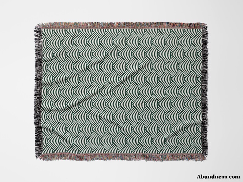 May include: A rectangular throw blanket featuring a repeating pattern of dark green and white semi-circles. The blanket has a fringed edge in black, brown, and red. The design is geometric and contemporary.