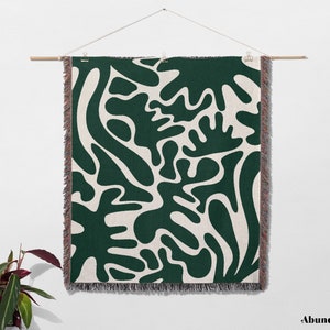 May include: A green and white woven wall tapestry with an abstract pattern of organic shapes. The tapestry has a fringe border.