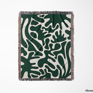 May include: A woven throw blanket with a green and white abstract pattern. The pattern features organic shapes and lines.