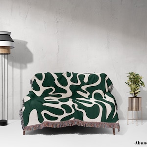 May include: A green and white throw blanket with a modern abstract pattern. The blanket has a fringe border and is draped over a couch.