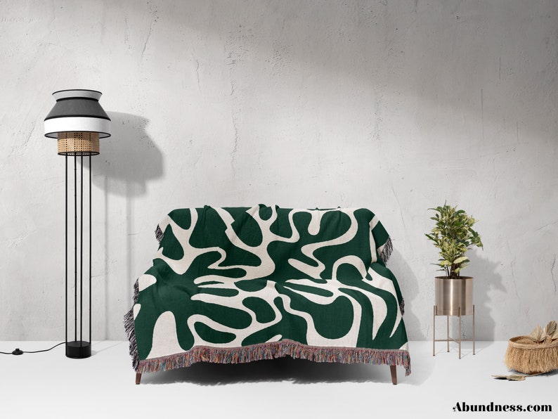 May include: A green and white throw blanket with a modern abstract pattern. The blanket has a fringe border and is draped over a couch.