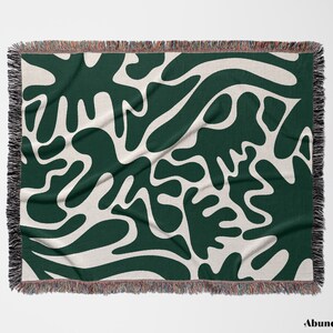 May include: A woven throw blanket with a green and white abstract pattern. The pattern features large, organic shapes that resemble leaves or branches.
