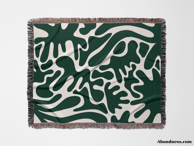 May include: A woven throw blanket with a green and white abstract pattern. The pattern features large, organic shapes that resemble leaves or branches.