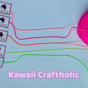 May include: Four spools of yarn in pink, orange, green, and yellow colors. The yarn is arranged in a line with the spools on the left and the yarn extending to the right. The yarn is labeled "Kawaii Craftholic".