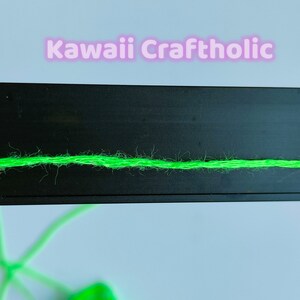 May include: A close-up of a bright green yarn strand on a black surface. The yarn is slightly fuzzy and has a subtle sheen.