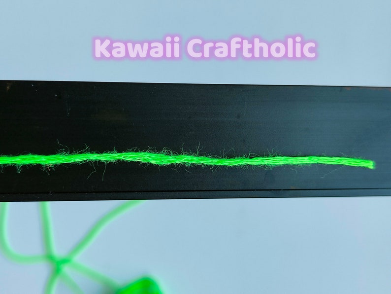 May include: A close-up of a bright green yarn strand on a black surface. The yarn is slightly fuzzy and has a subtle sheen.