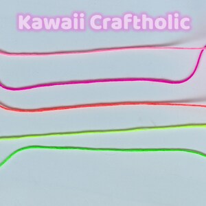 May include: Four strands of colorful embroidery floss are laid out on a white surface. The floss colors are pink, magenta, orange, and neon green. The text "kawaii Craftholic" is written in pink letters above the floss.