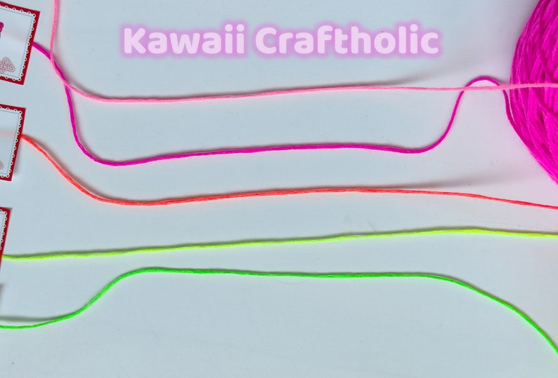 May include: Four strands of colorful embroidery floss are laid out on a white surface. The floss colors are pink, magenta, orange, and neon green. The text "kawaii Craftholic" is written in pink letters above the floss.