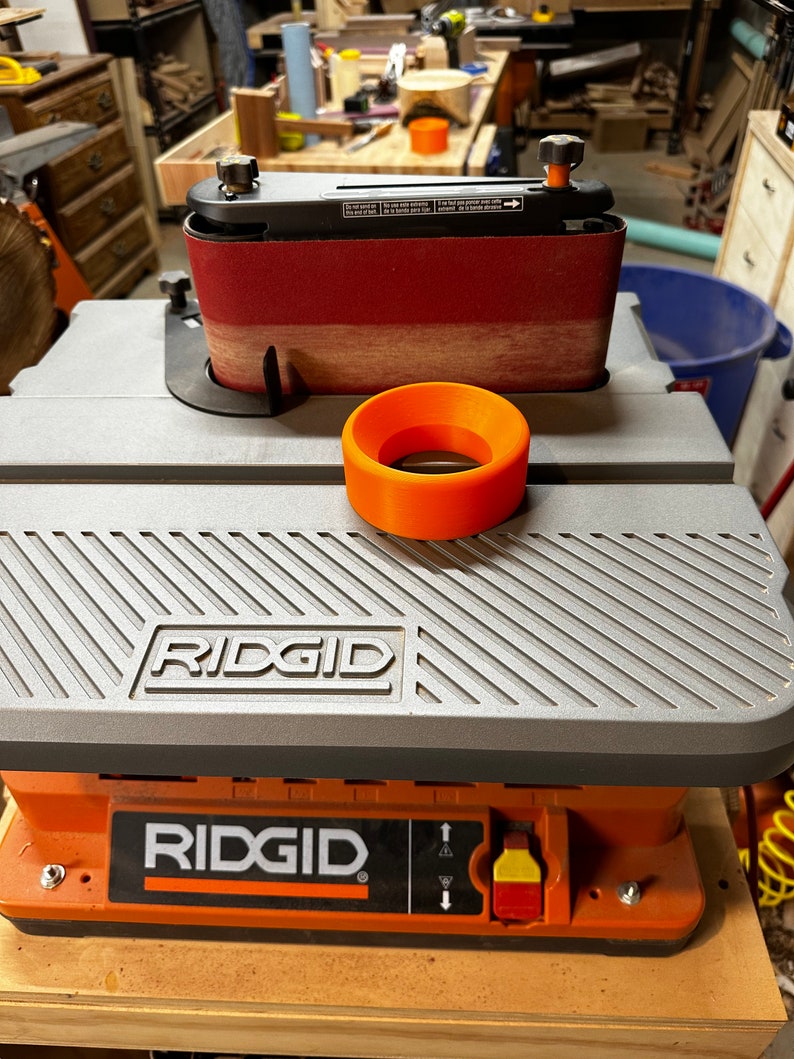 May include: A gray and orange Ridgid belt sander with a sanding belt and a round orange sanding guide. The sander has a black power switch with a red and yellow button.