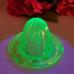 Può includere: Uno spremiagrumi in vetro verde con una parte superiore scanalata e una base larga. Lo spremiagrumi è fatto di vetro all'uranio e brilla sotto una luce nera.