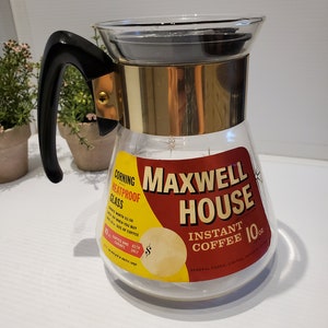 May include: A vintage glass coffee carafe with a black handle and gold trim. The carafe is labeled "Maxwell House Instant Coffee 10 oz." and "Corning Heatproof Glass".